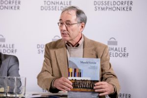 Georg Lauer stellt in der PK zum Jubiläum das Festbuch "MusikVereint" vor.
