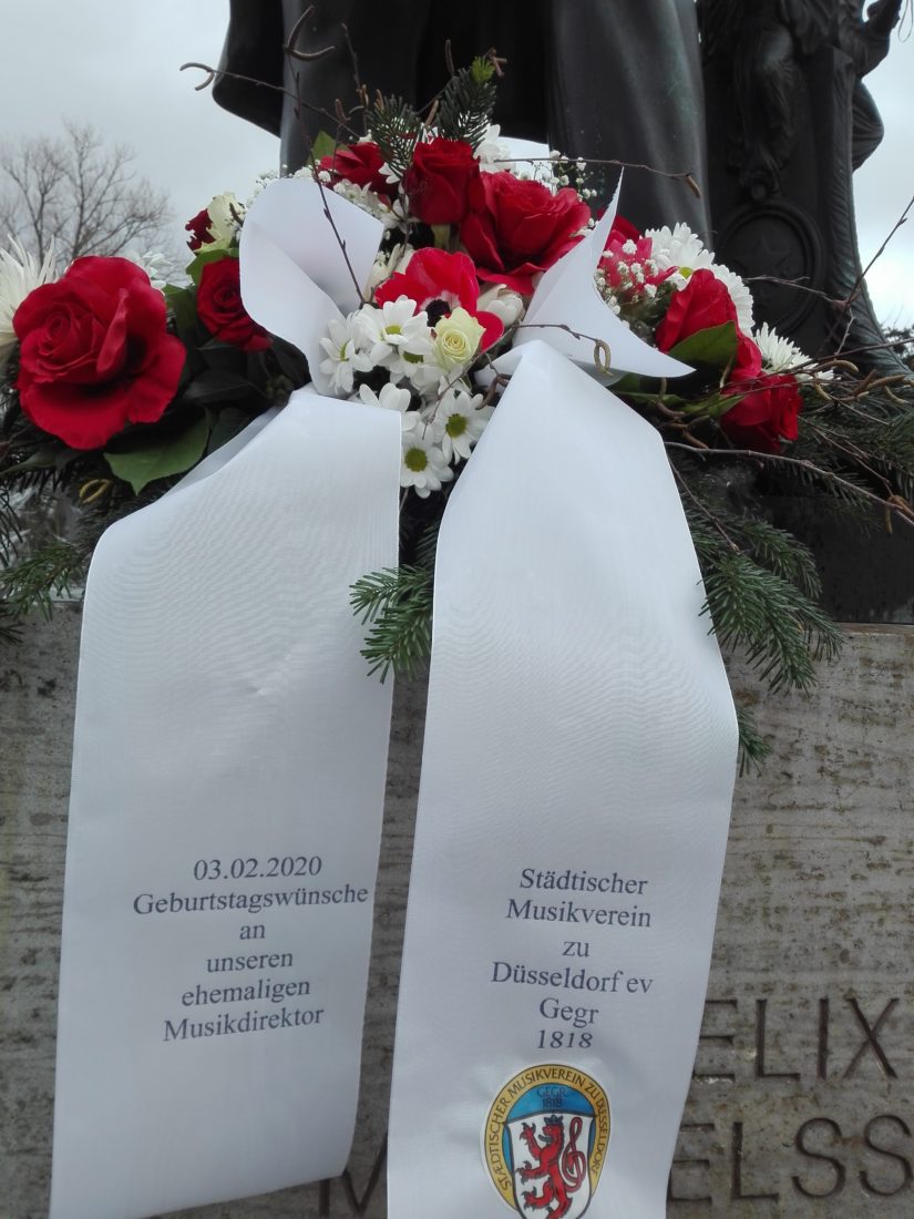 Der Städtische Musikverein erinnert am 3.2.2020 an den Geburtstag seines ehemaligen Musikdirektors mit einem Blumengesteck an seinem Denkmal