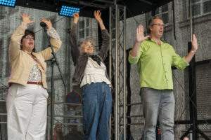 14.6.2026 Art:walk auf der Straße der Romantik und Revolution, der Bilker Straße. Auf der Bühne die Singleiterinnen Maria Carreras und Clementine Schwander und der Singleiter Martin Lucaß schwer im Einsatz.